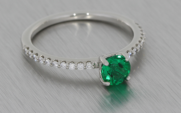 Dainty platinum ring set with a round emerald and diamond shoulders